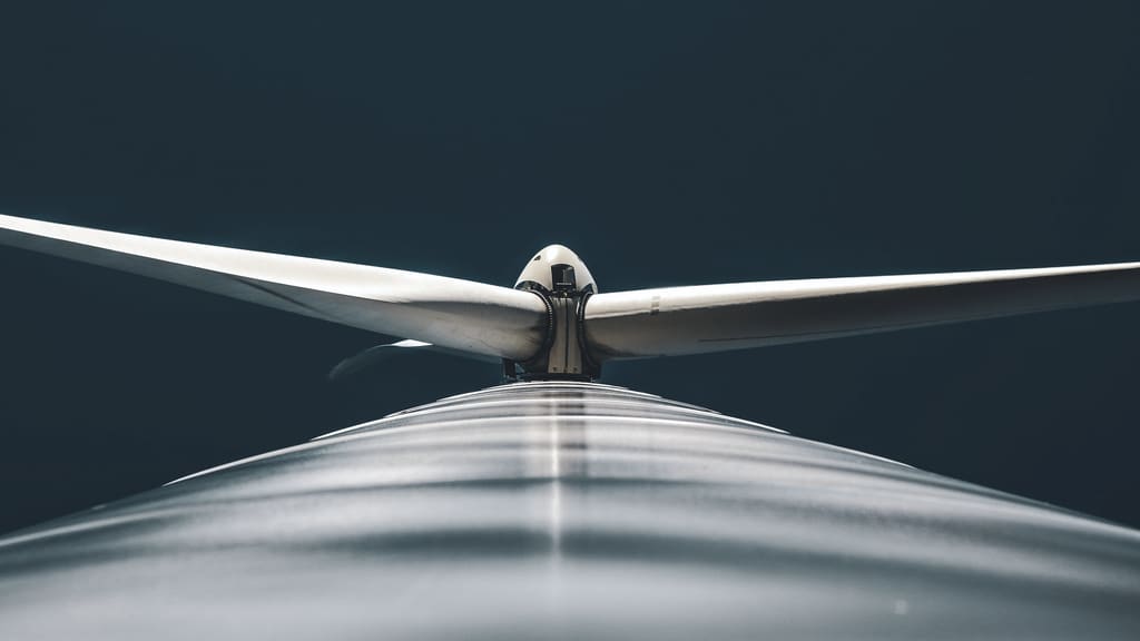 Looking along the top of a wind turbine nacelle towards its blades against a dark sky