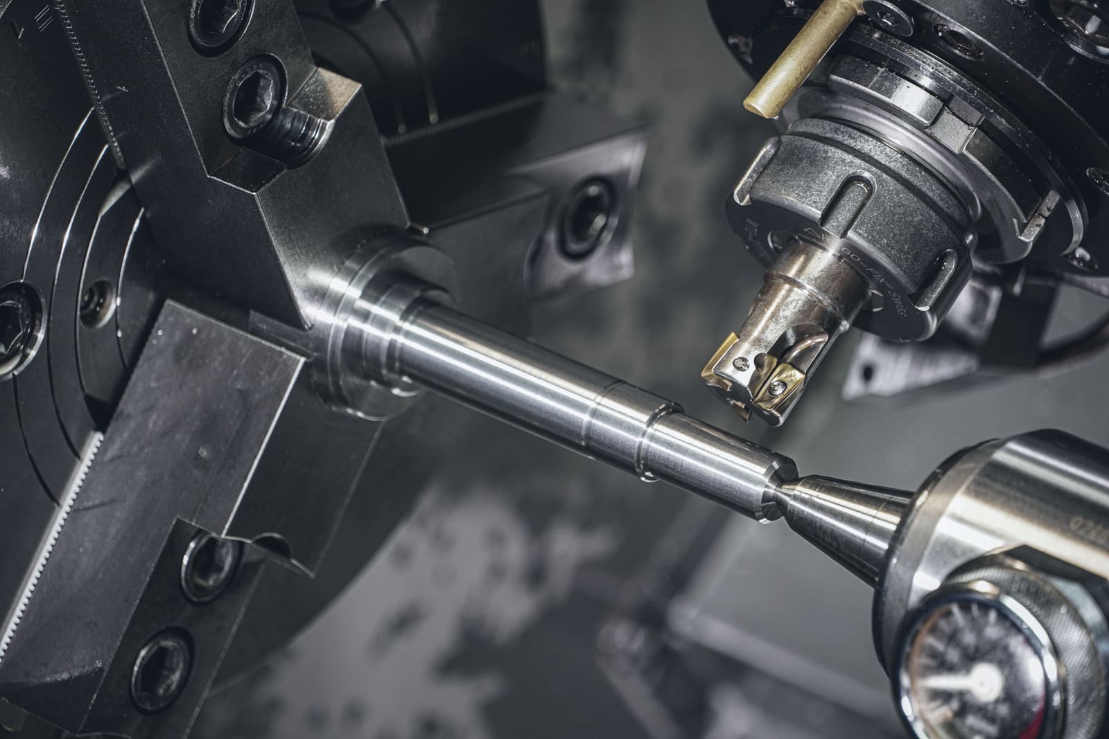 A titanium shaft being turned between a lathe chuck and a live centre, an indexable milling cutter poised above it