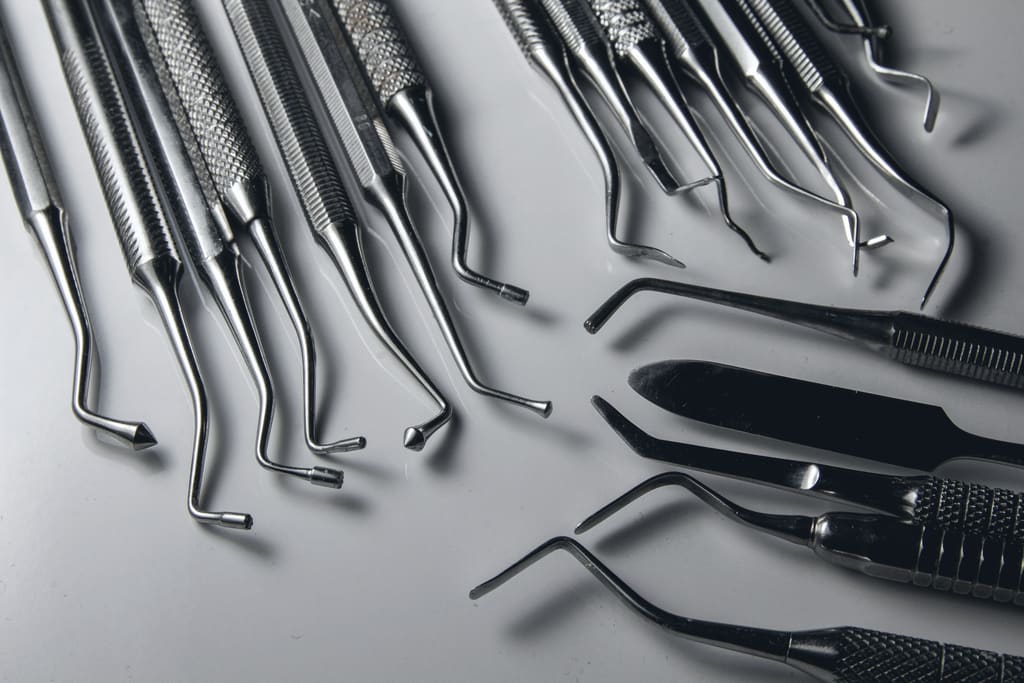 Polished stainless surgical instruments laid in rows on a grey surface