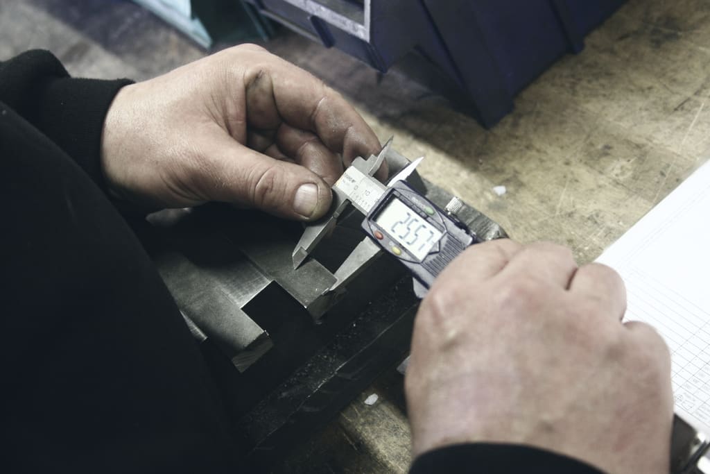Hands measuring a machined part with a digital caliper