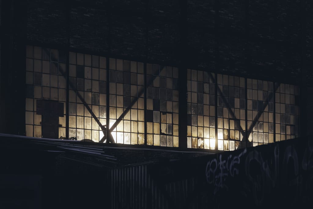 Light glowing through the steel-framed windows of an industrial building at night