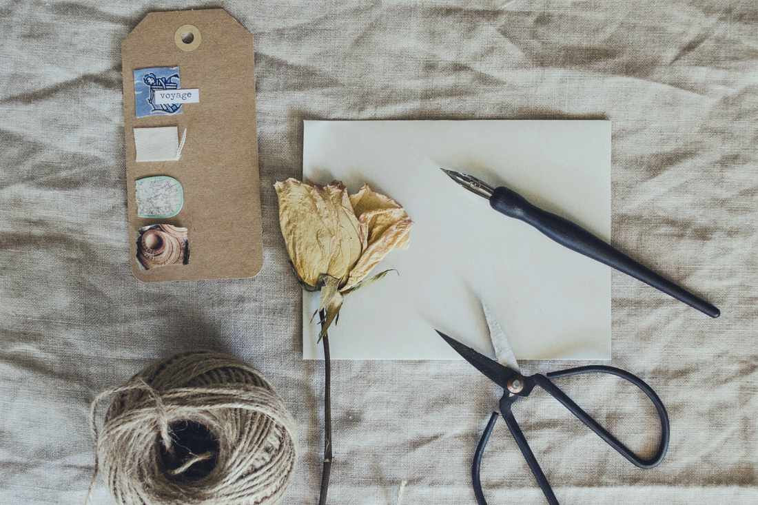 A kraft gift tag, cotton twine, scissors and a pen laid out on washed linen