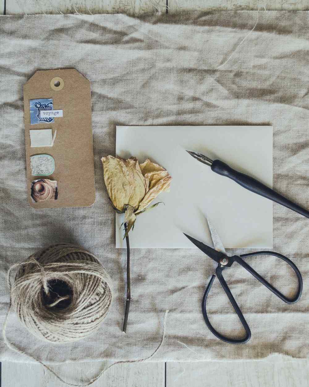 A kraft gift tag, a hank of cotton twine, scissors and a pen laid out on washed linen