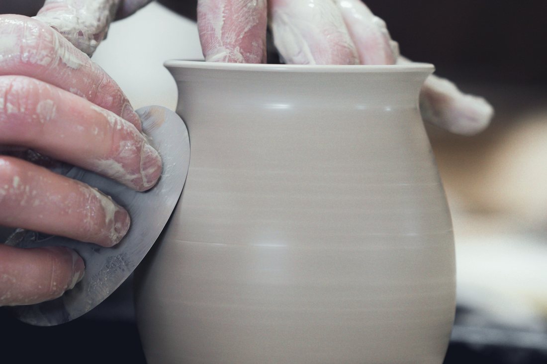 Hands shaping a pot on a turning wheel
