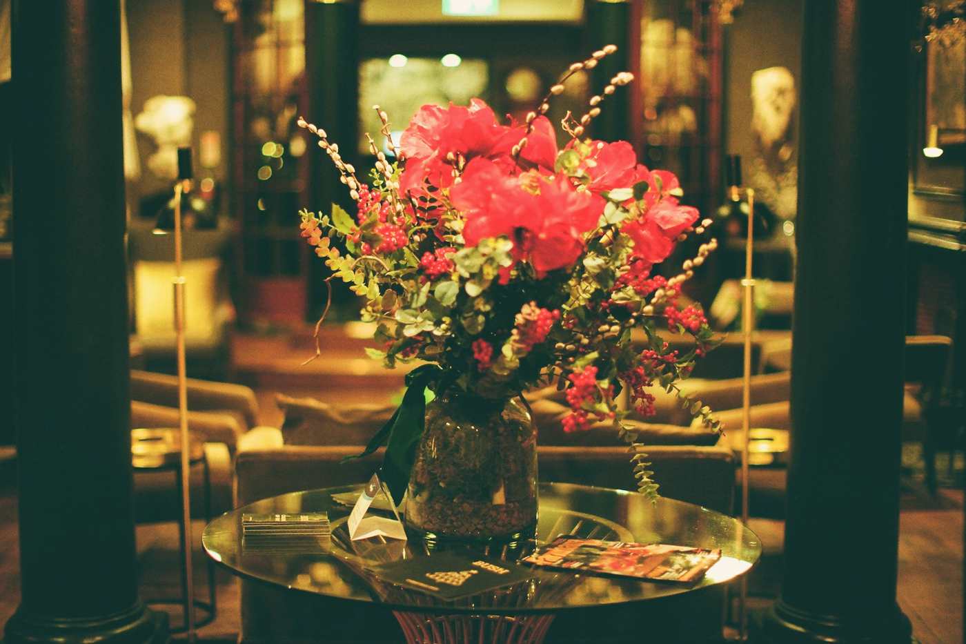 A big vase of red flowers on a glass table in a hotel lobby