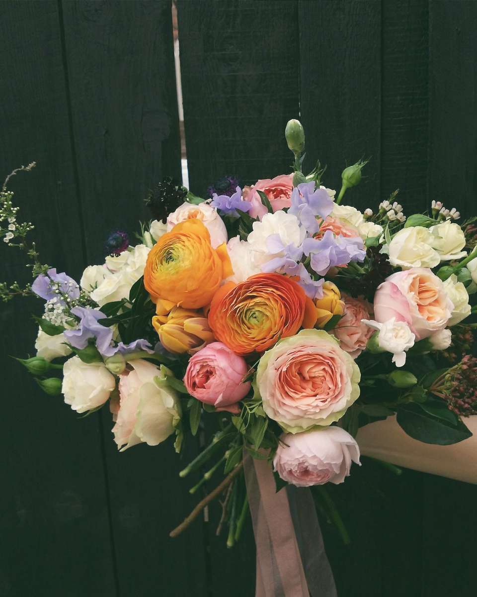 A hand holding the Larkmead bouquet of orange ranunculus and peach roses