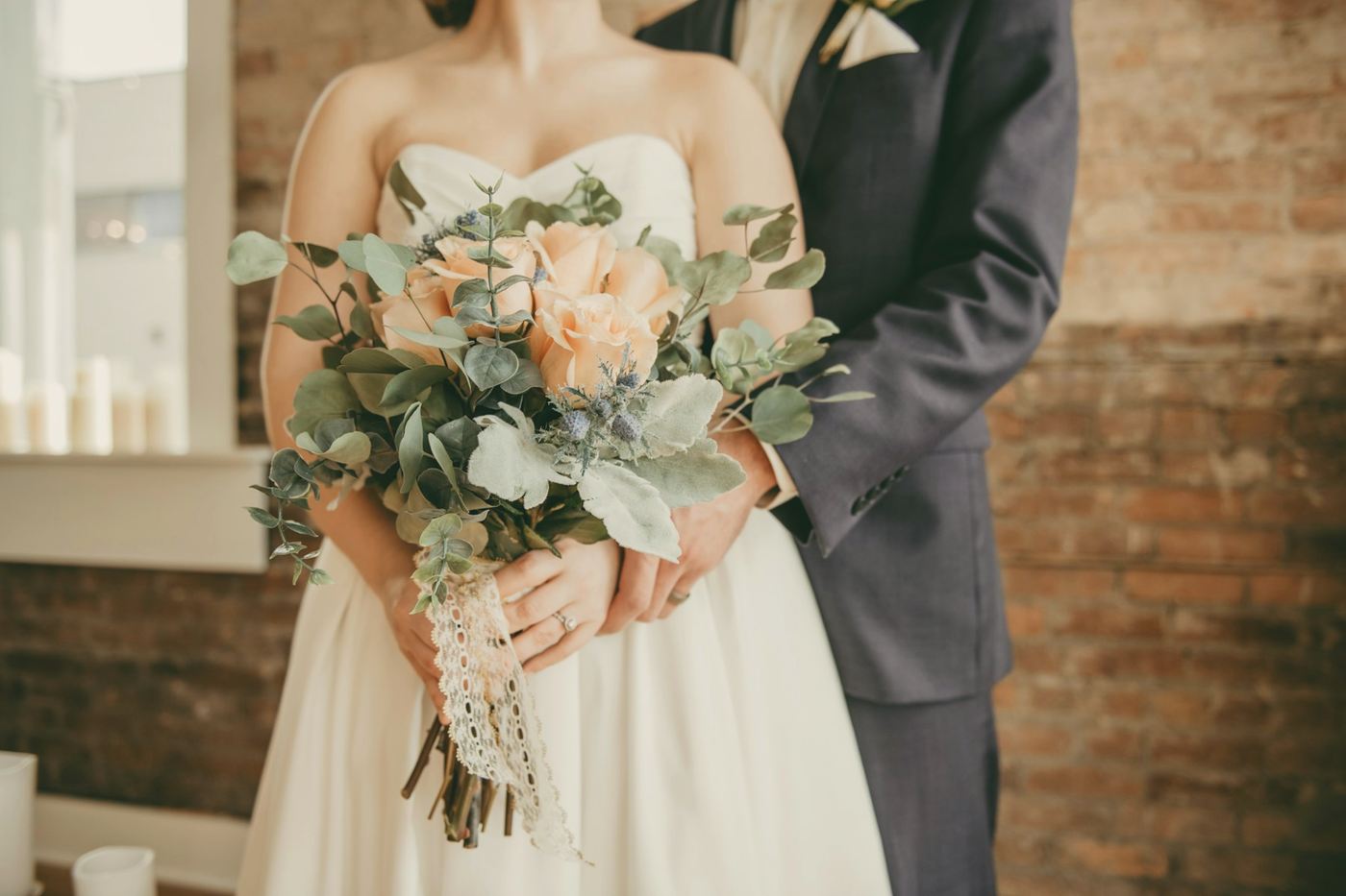 A bride and groom, the bride holding a soft bouquet of peach roses and eucalyptus