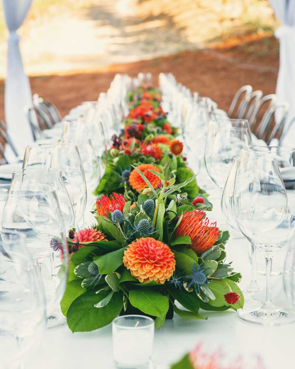 A table runner of orange and red flowers between rows of glasses