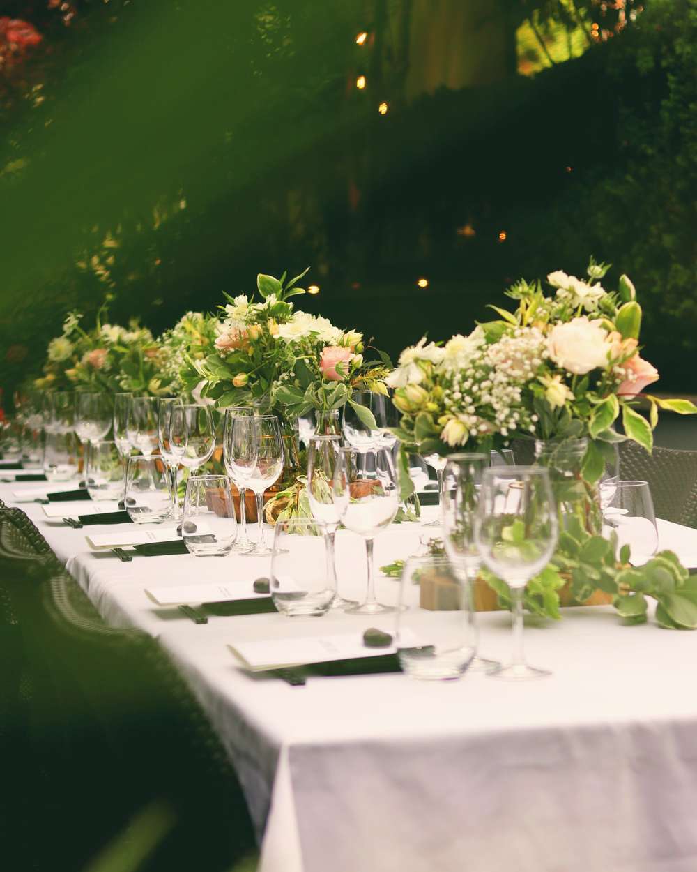 A long candlelit wedding table with low garden arrangements under trees