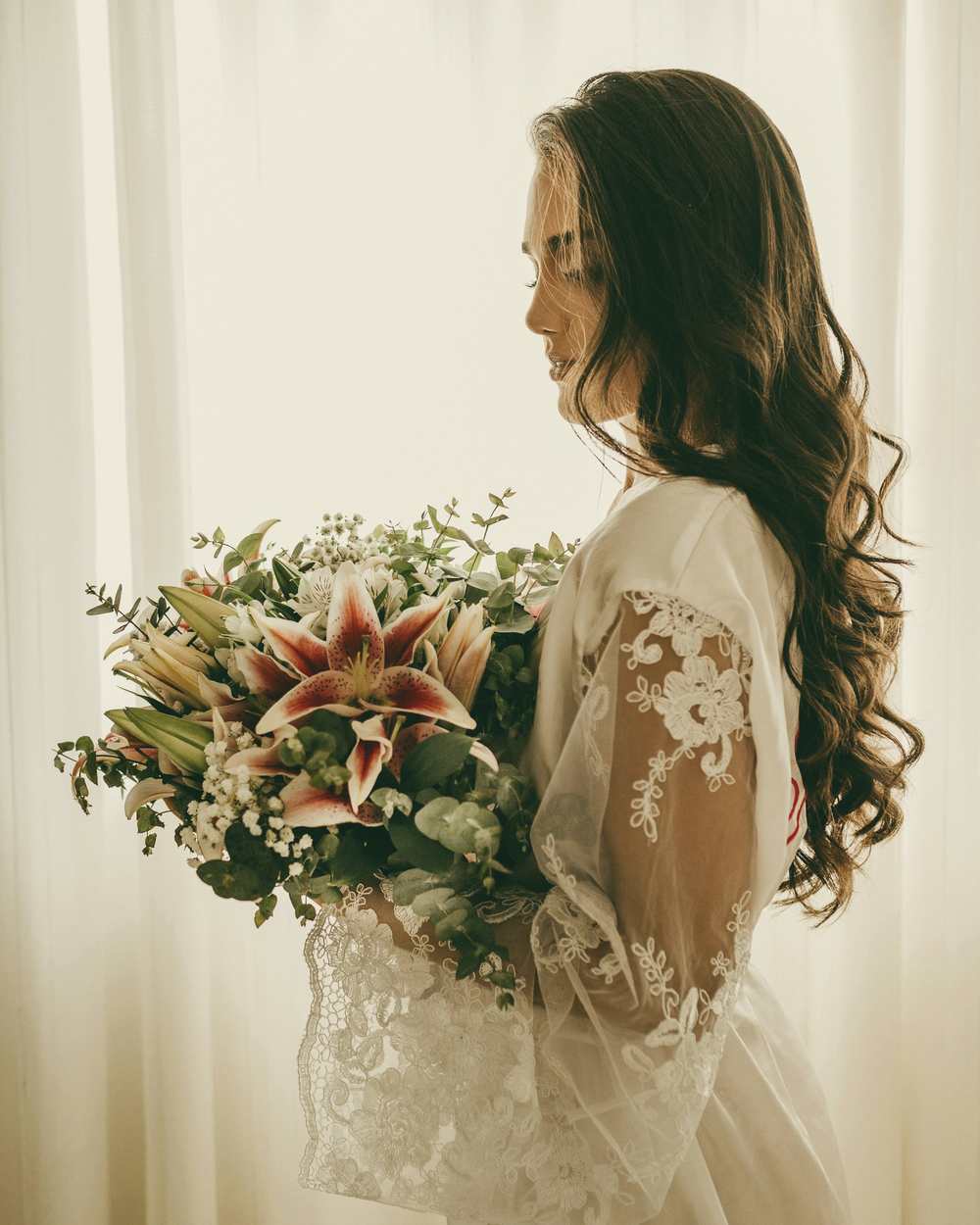 A bride by a window holding a loose garden bouquet