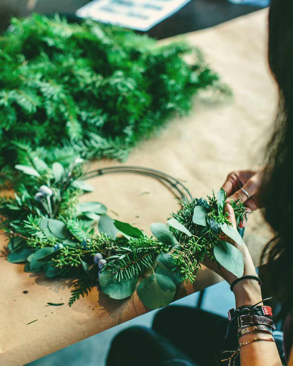 Hands shaping a fresh green wreath on a wooden table