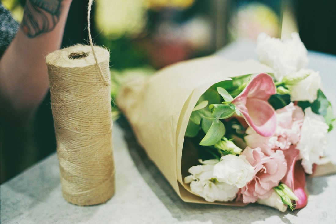 A bouquet wrapped in paper beside a spool of twine on the workbench