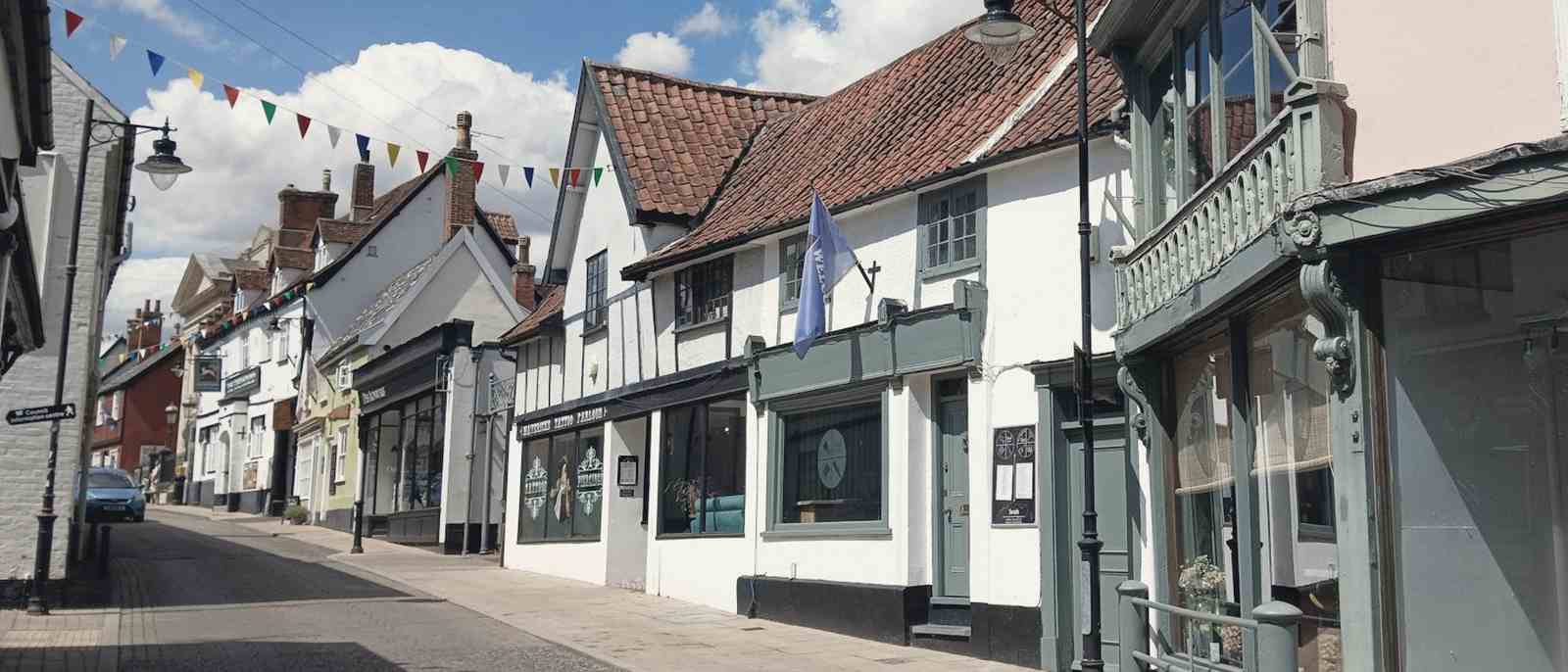 A quiet market-town street of white-painted shops under a line of bunting