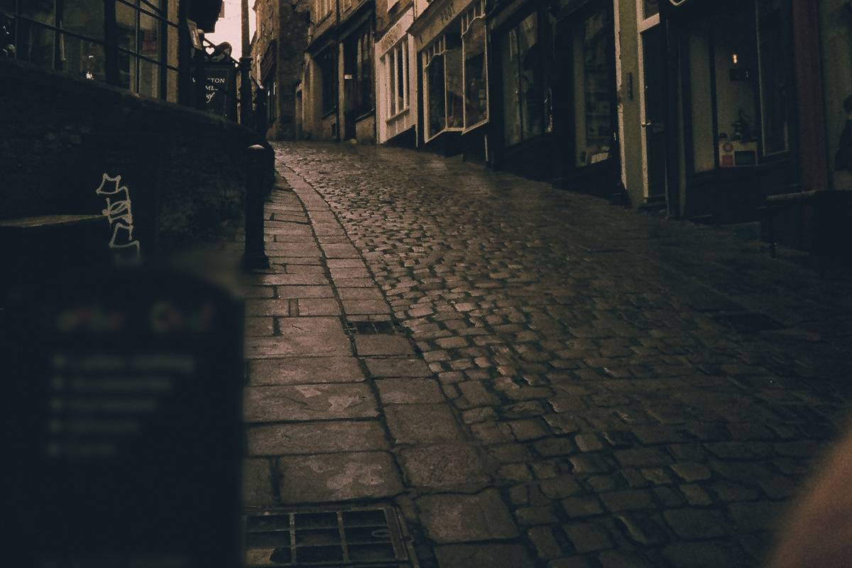A narrow cobbled lane of old shops at dusk under a pink sky