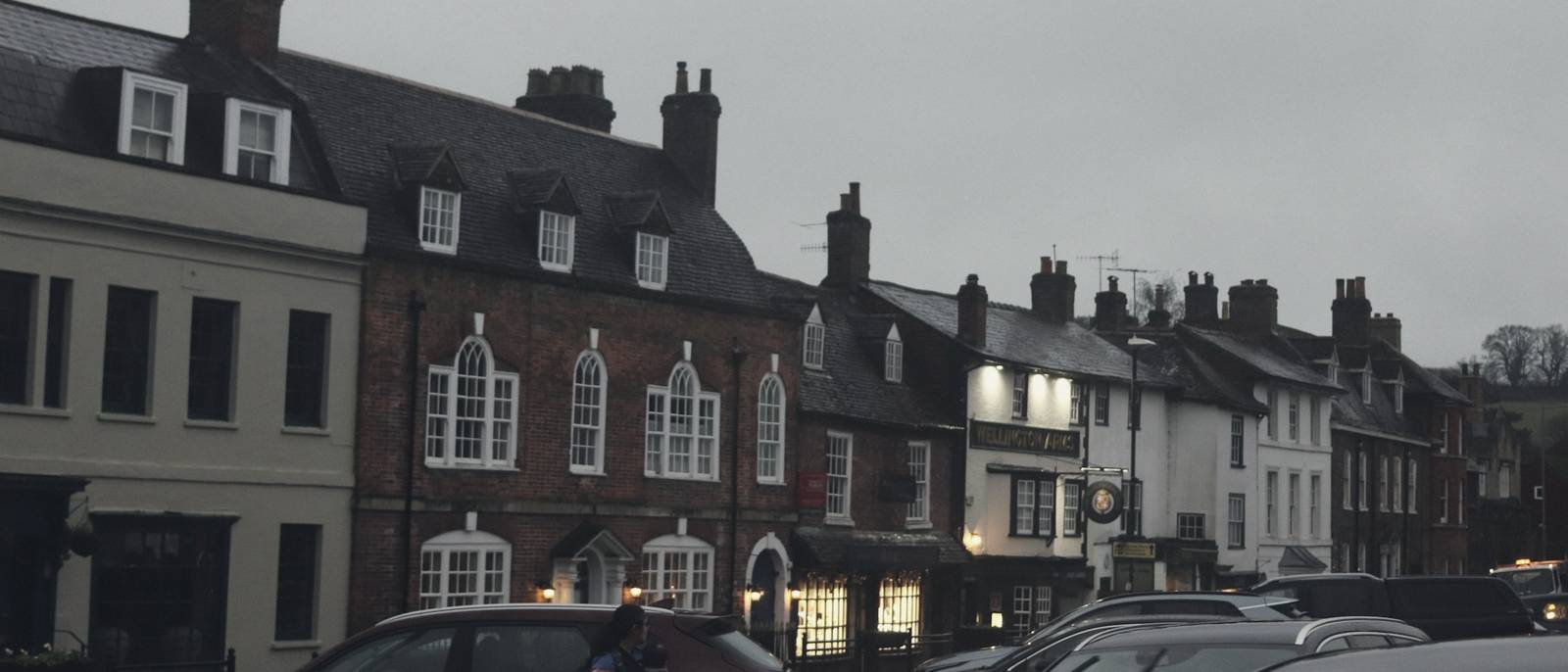 Georgian brick buildings around a town square at dusk, with lit windows