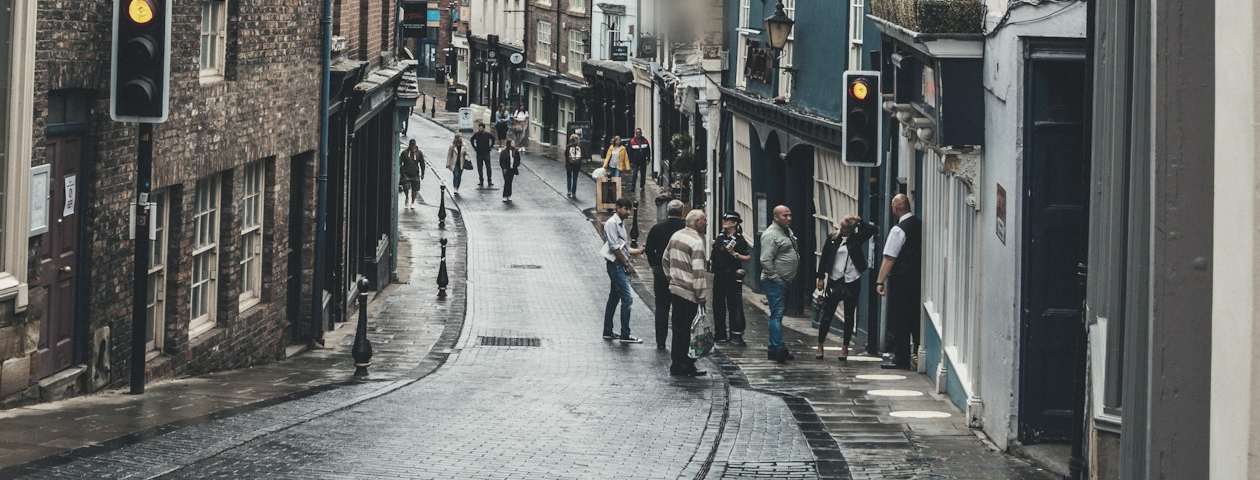 A rain-wet cobbled shopping street with neighbours stopping to talk on the pavement