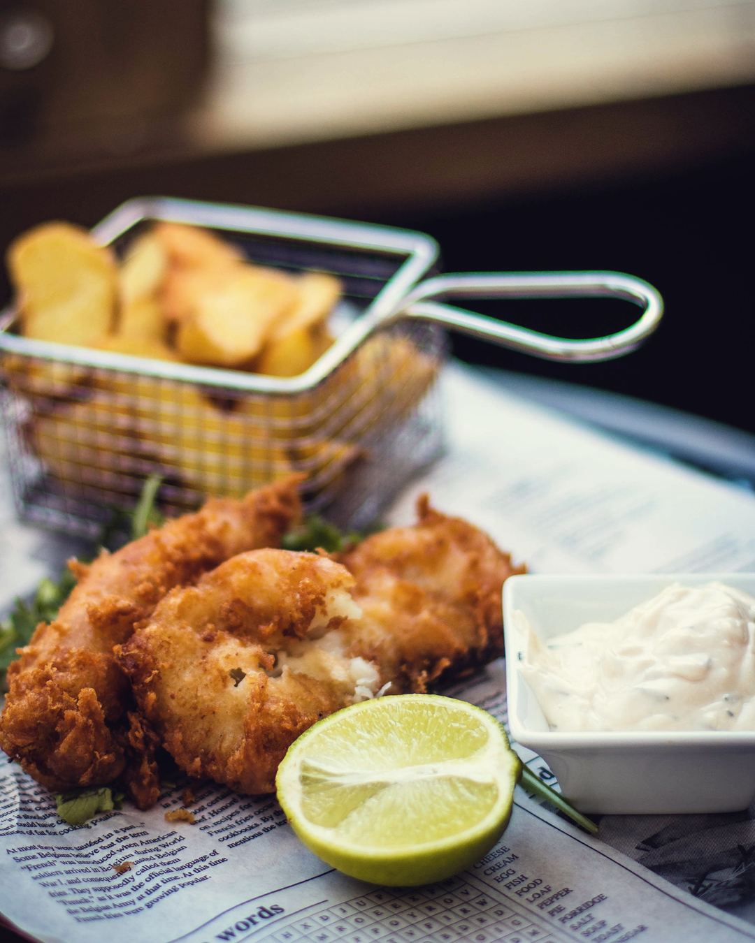 Battered cod and chips on paper with tartare sauce and a wedge of lime