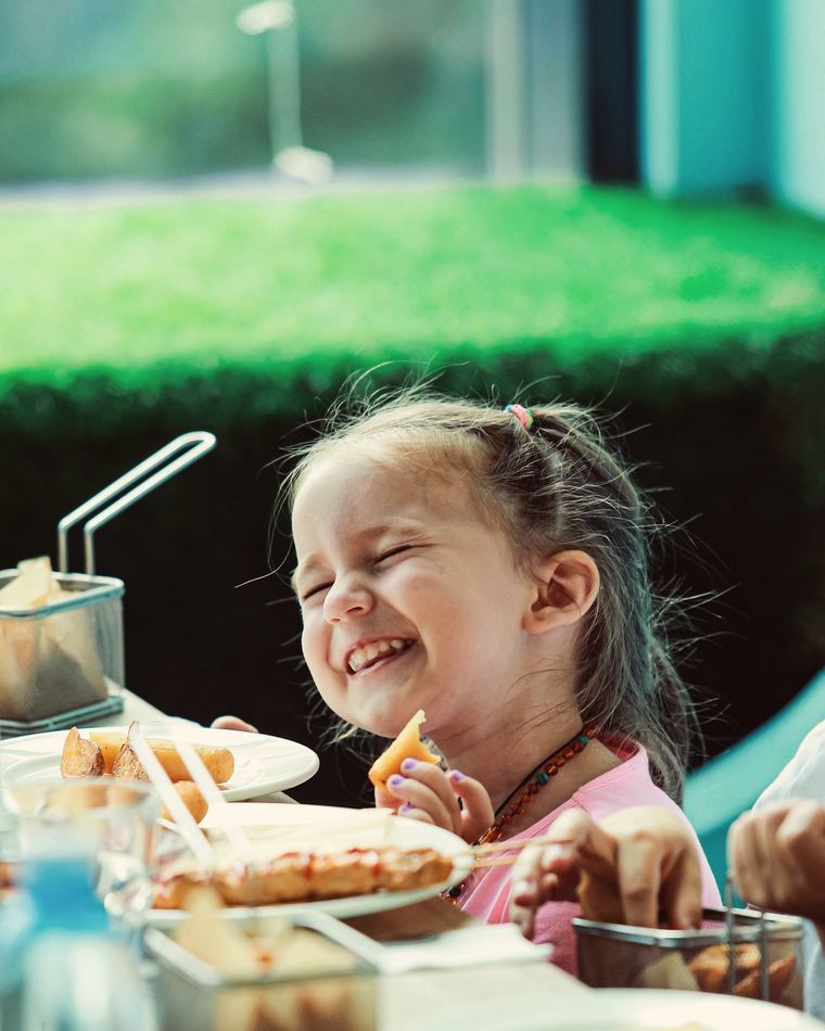 A laughing girl eating chips from a basket at a table