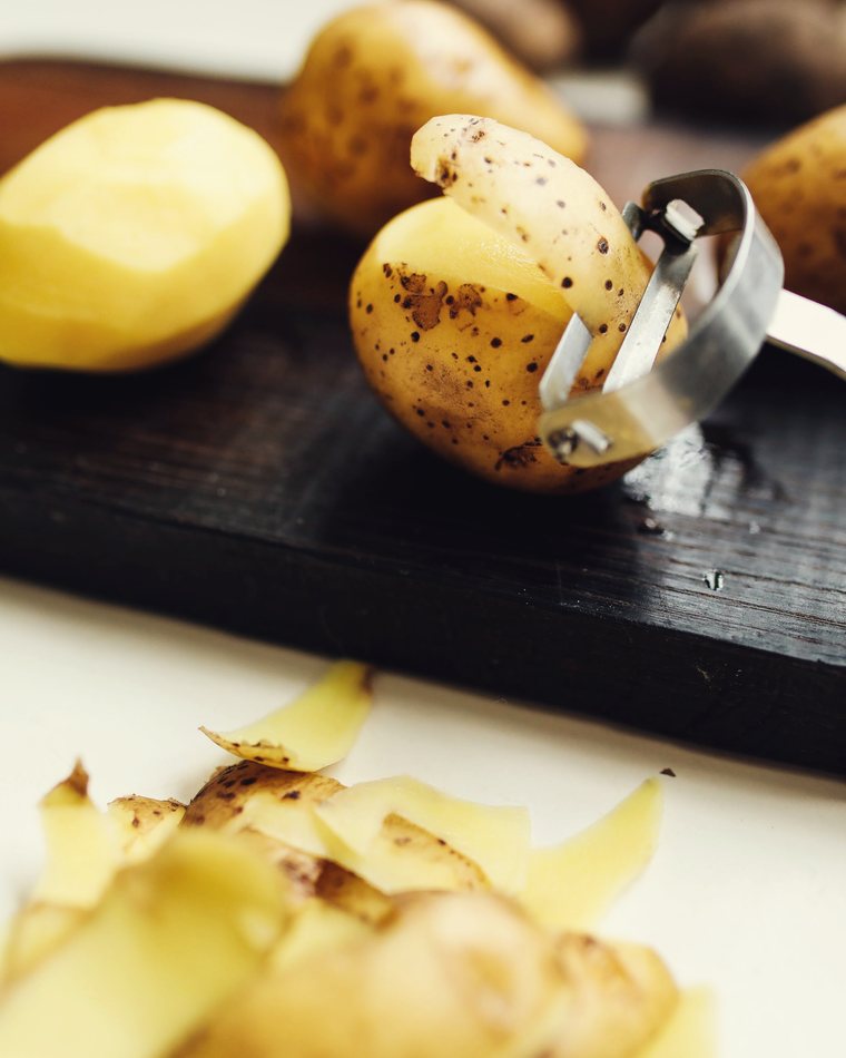 Potatoes being peeled on a dark board
