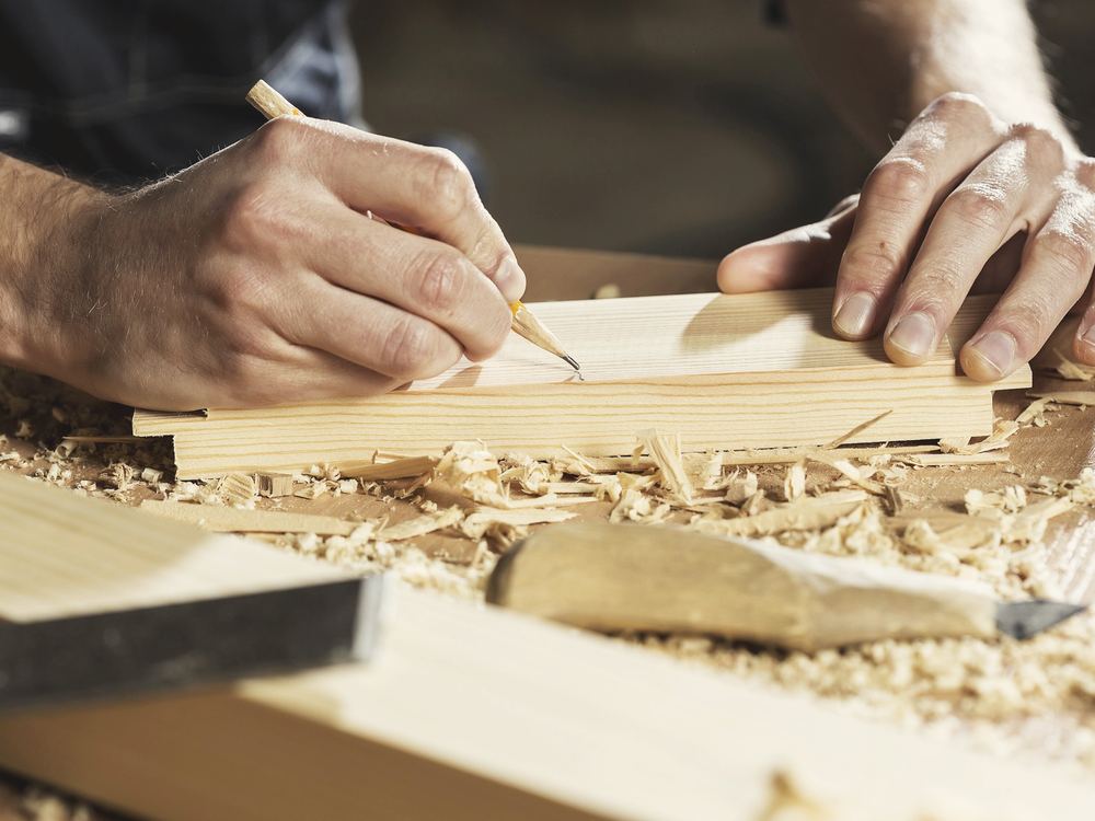 A carpenter marking a timber board with a pencil among wood shavings