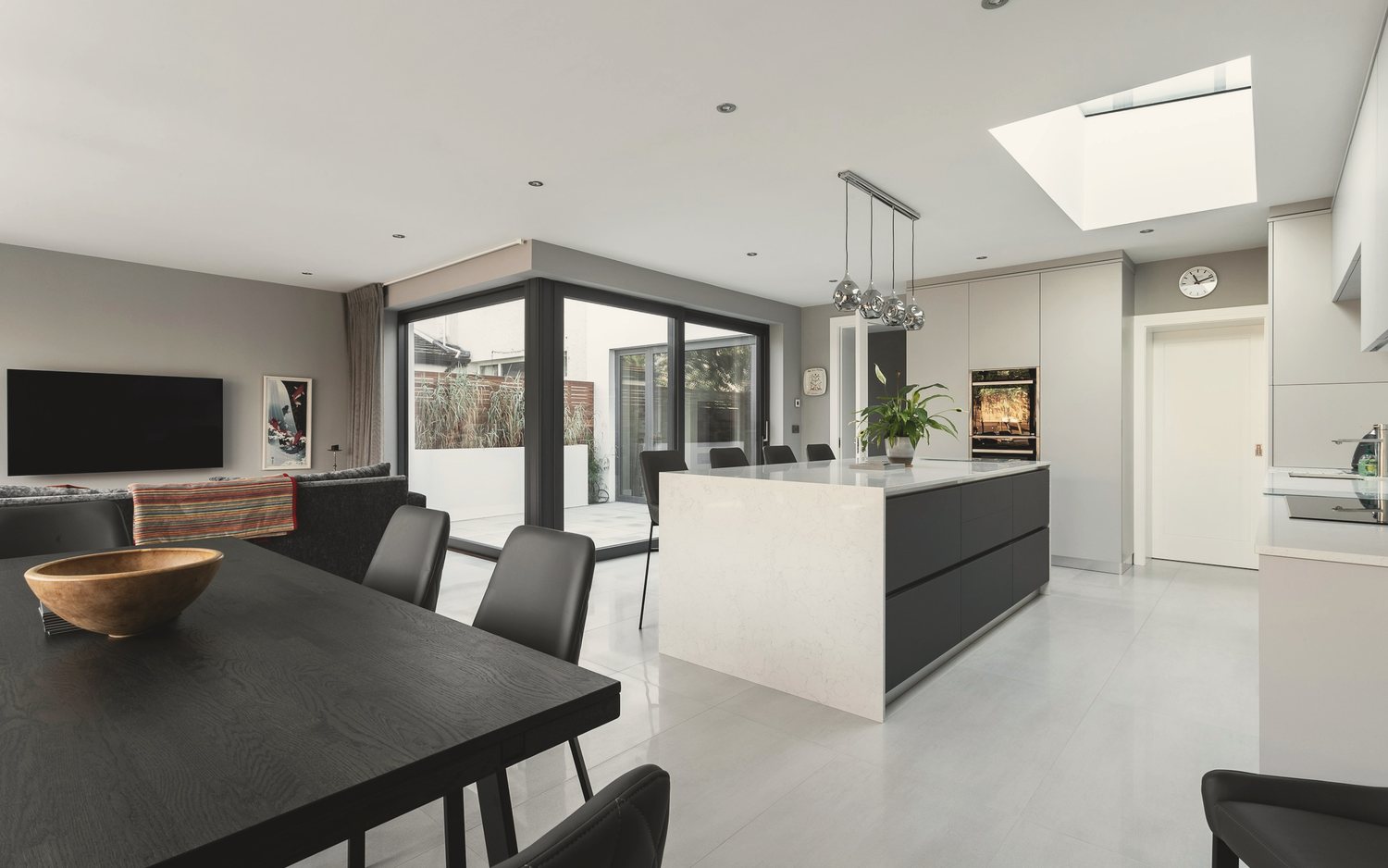 Finished rear kitchen extension with a rooflight over a white island, dark-framed sliding doors to the garden and a polished grey floor
