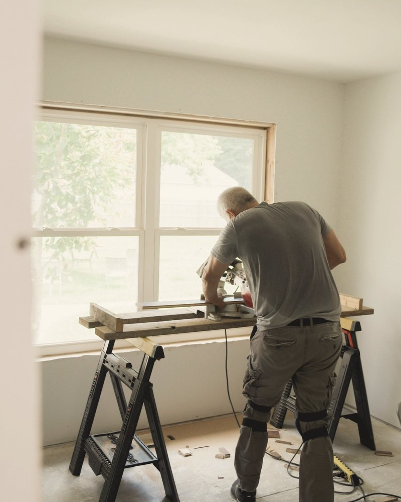 A builder cutting timber on a sawhorse in a bright room being renovated