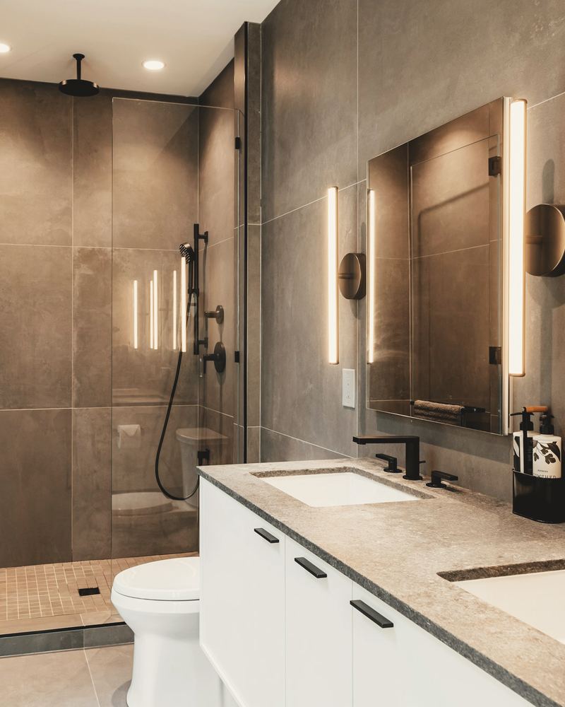Bathroom with large stone-effect tiles, a glass walk-in shower and lit mirror