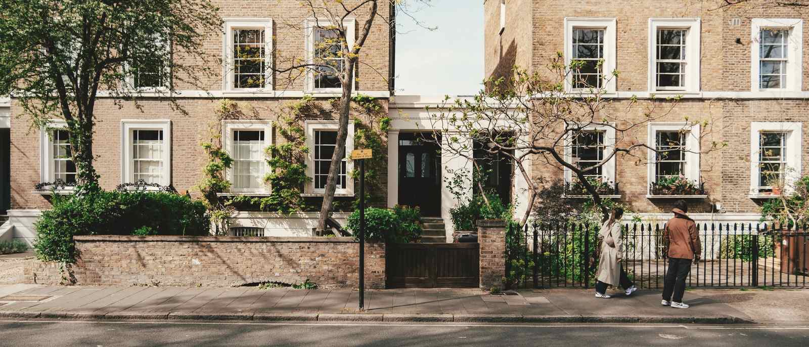 A street of brick Victorian terraced houses with trees and front gardens