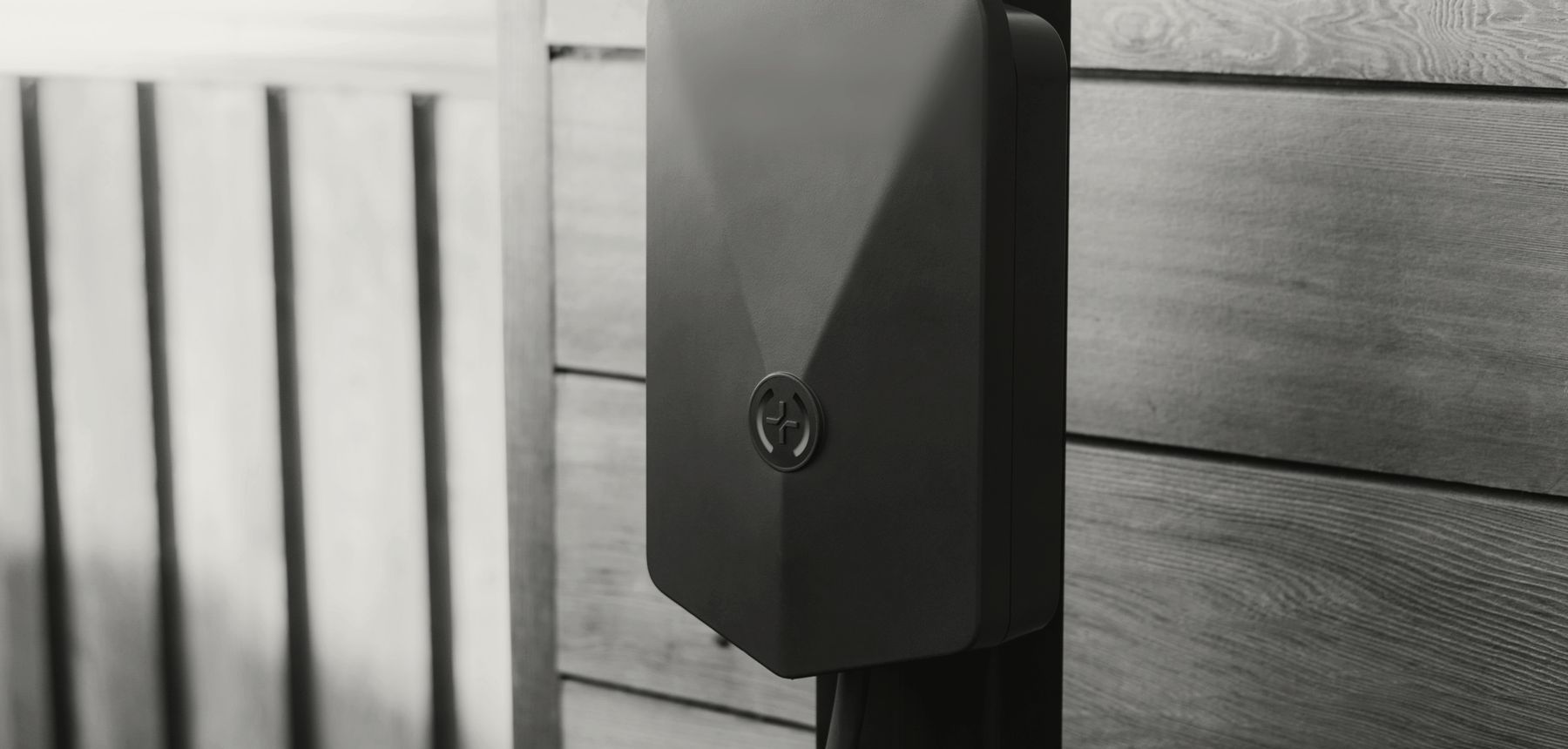 A dark home EV charger mounted on timber cladding, its status light glowing
