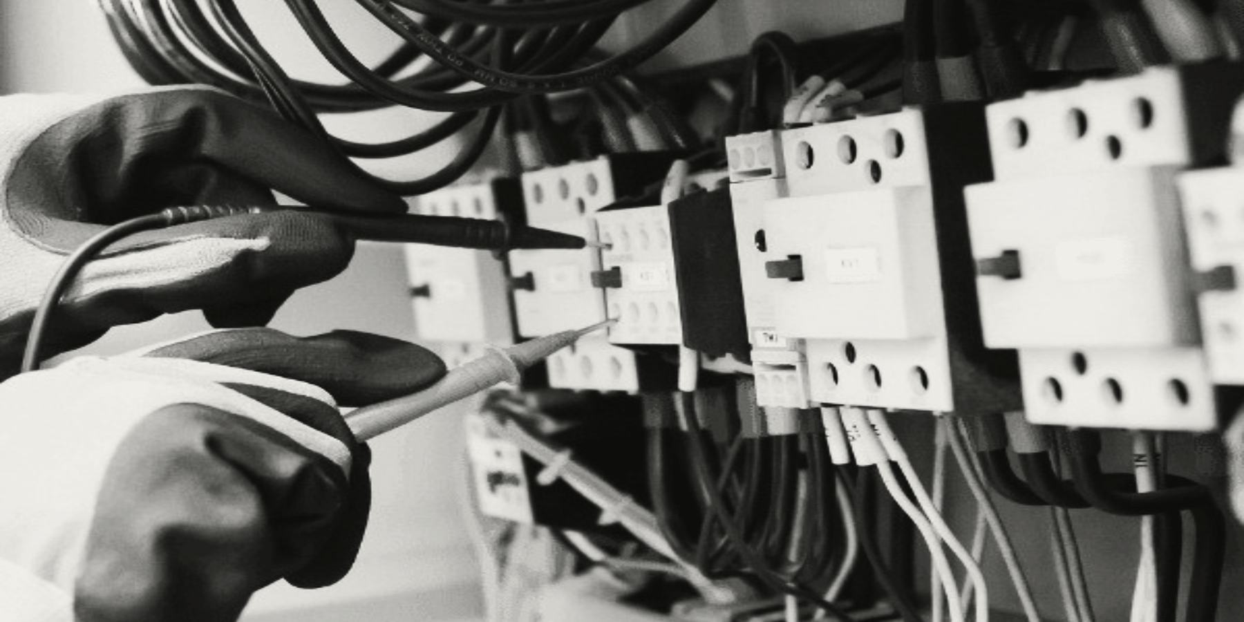 An electrician in gloves testing terminals in a board with a probe