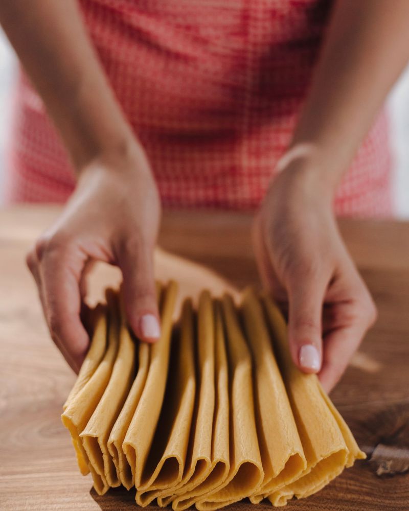 Hands folding a sheet of fresh pasta dough into layers before cutting