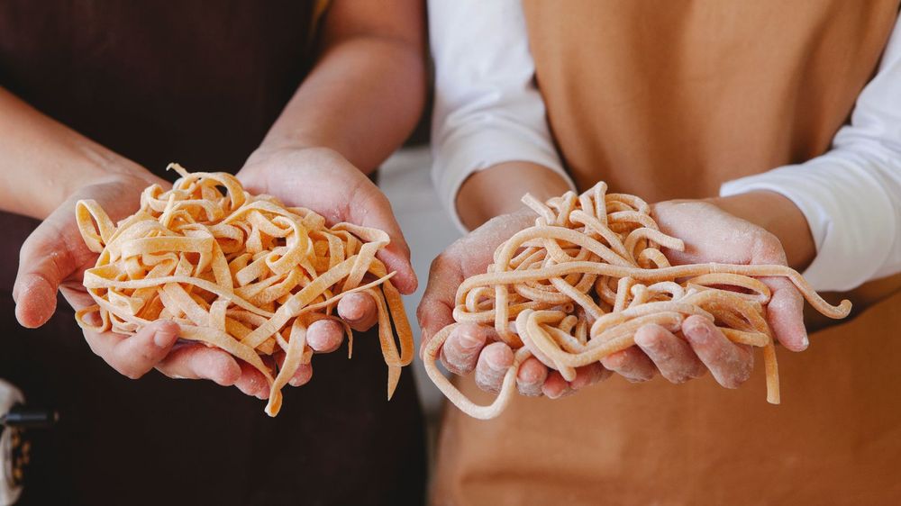 Two pairs of hands holding nests of fresh egg tagliatelle and pici