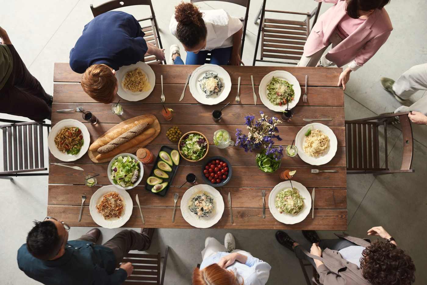 Seen from above, a long wooden table shared by a big group, covered in plates of pasta, salads and bread
