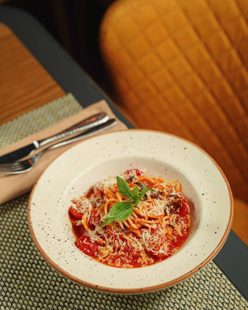 A bowl of pasta in tomato sauce topped with grated cheese and a basil sprig on a speckled plate