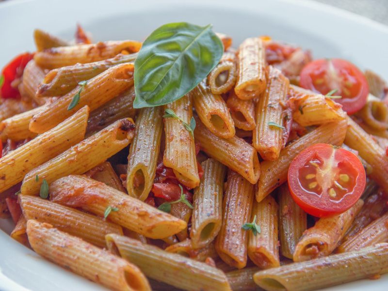 Penne in a bright tomato sauce with cherry tomatoes and a basil leaf