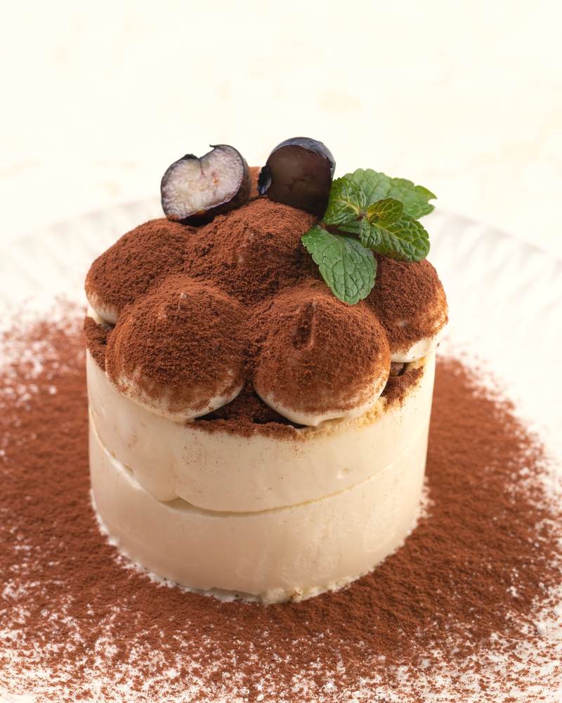 A round of tiramisu dusted with cocoa, topped with chocolate and a mint leaf